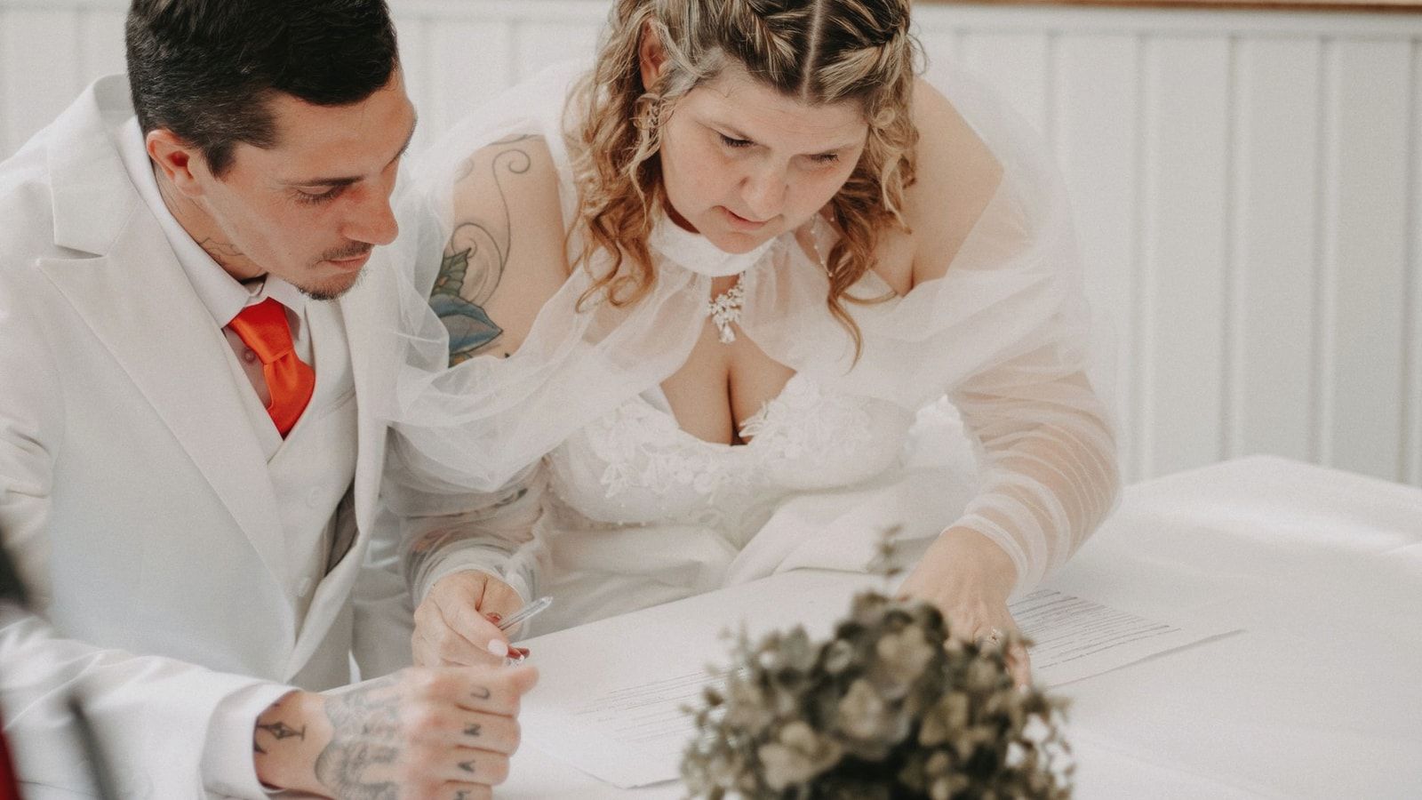 A bride and groom sign their marriage certificate during a beautiful indoor wedding ceremony.
