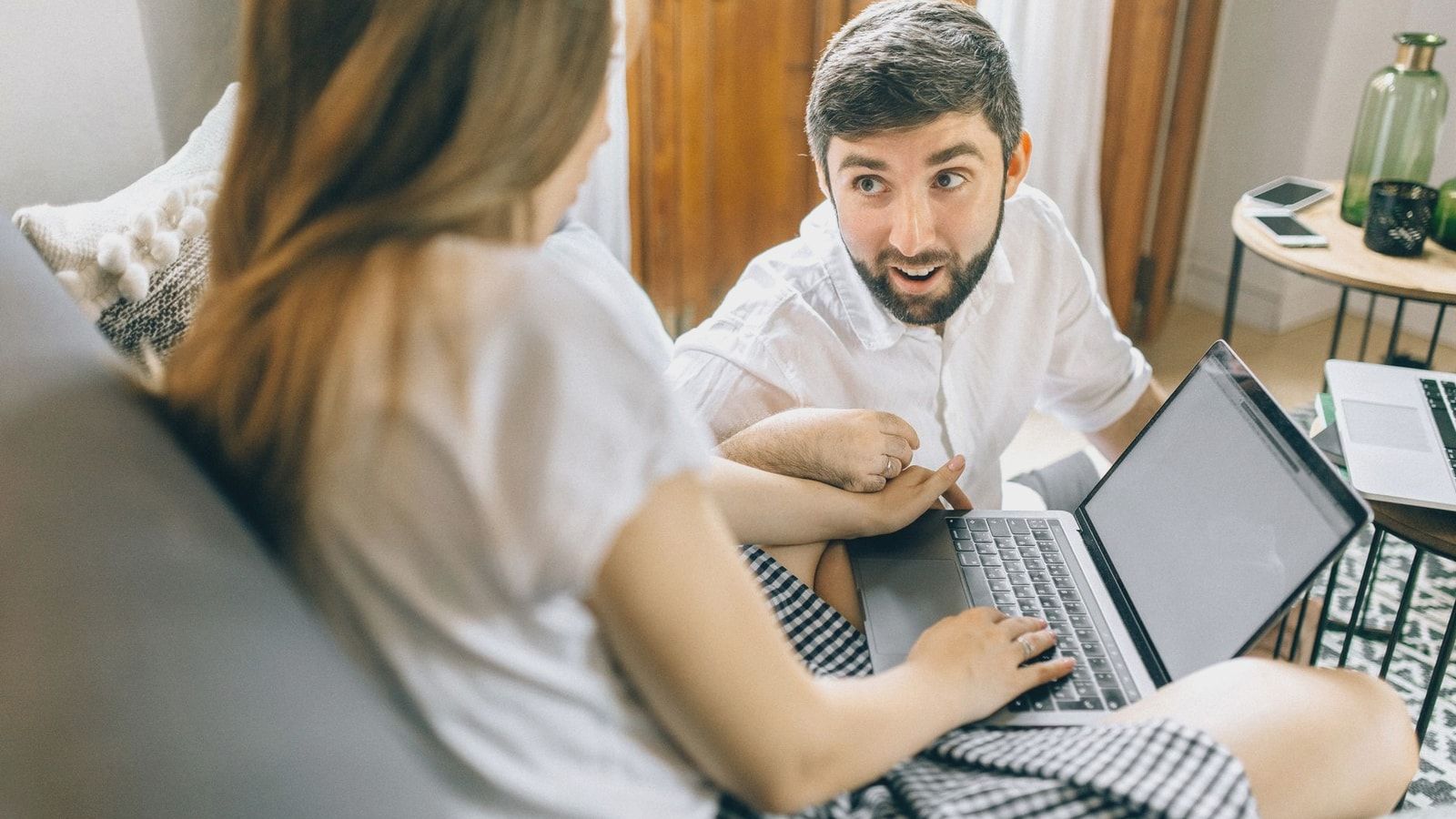 Couple working together from home on laptops, engaged in conversation.