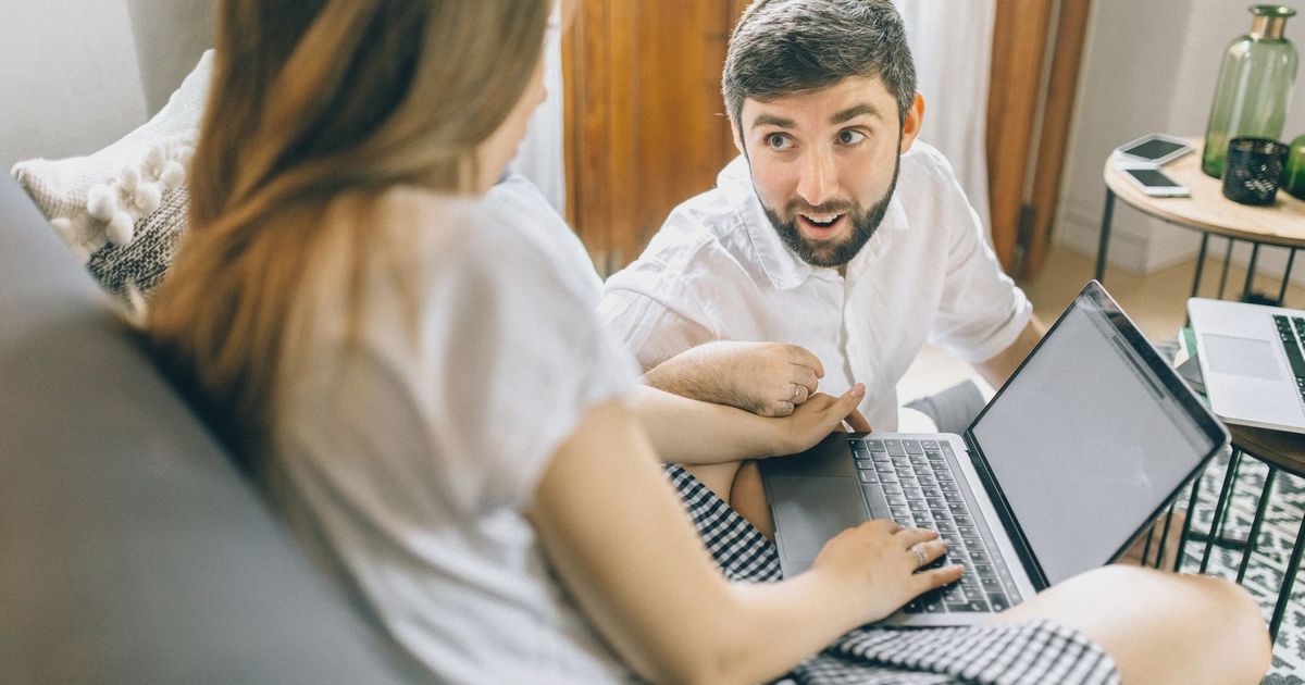 Couple working together from home on laptops, engaged in conversation.