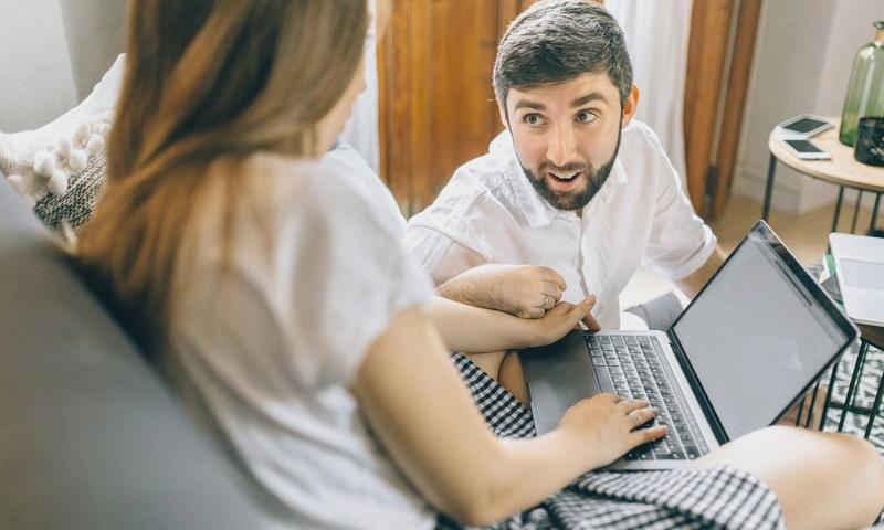 Couple working together from home on laptops, engaged in conversation.