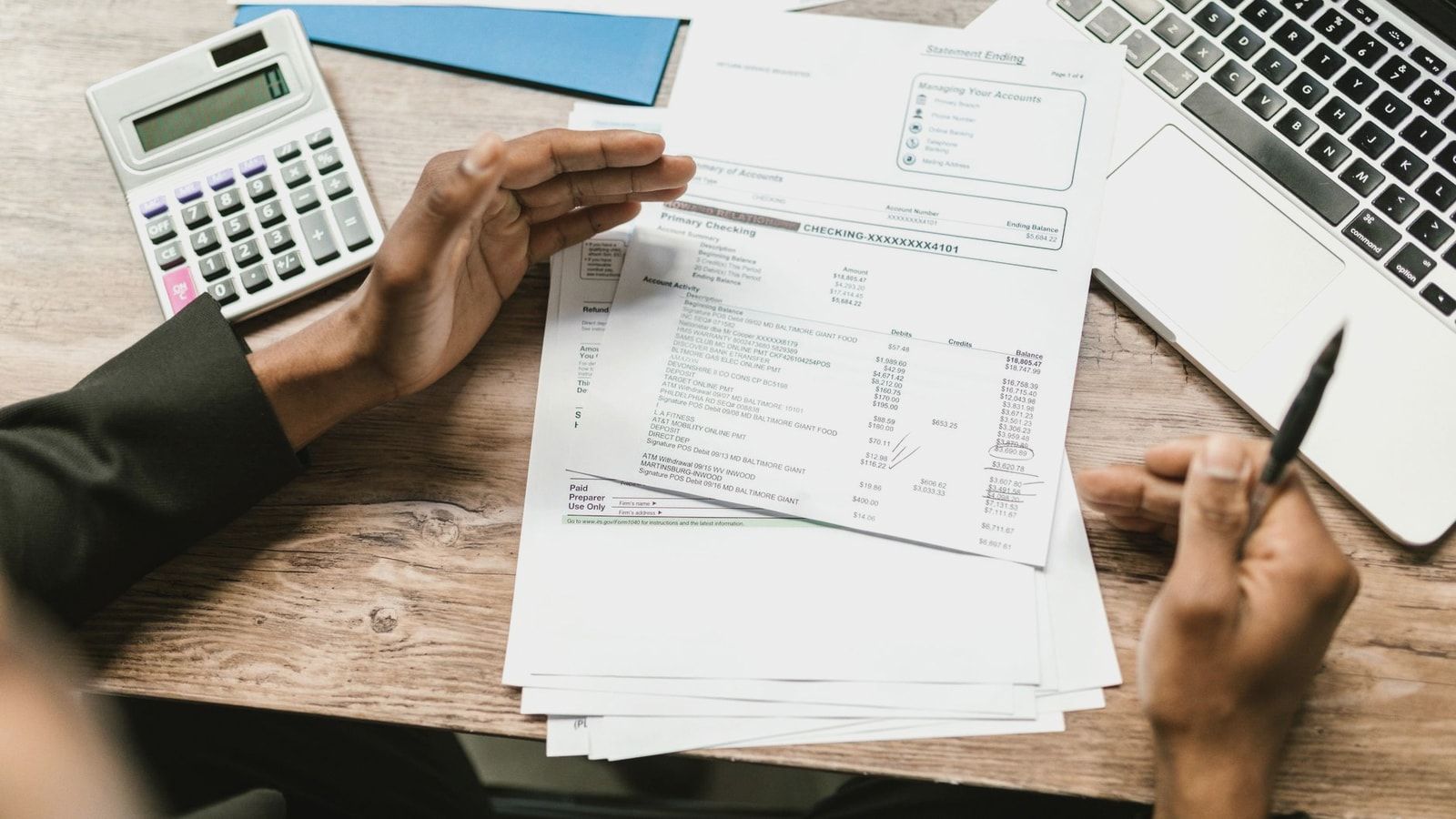 Hands holding financial documents with calculator and laptop on office desk, business analysis scene.
