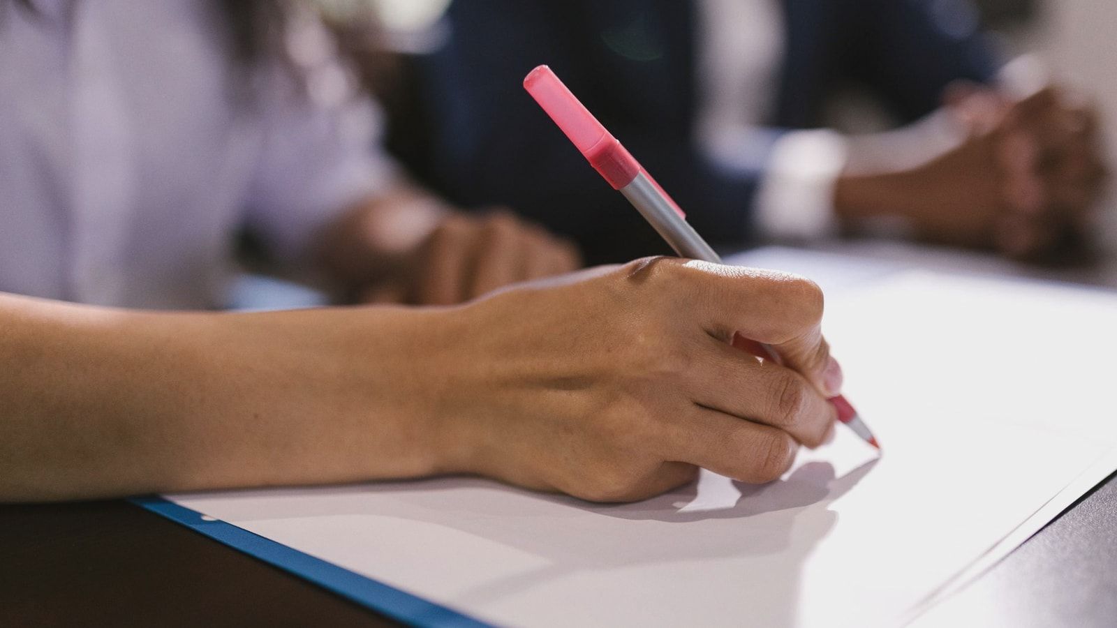 Detailed close-up of a person writing on paper with a pen in an office setting.