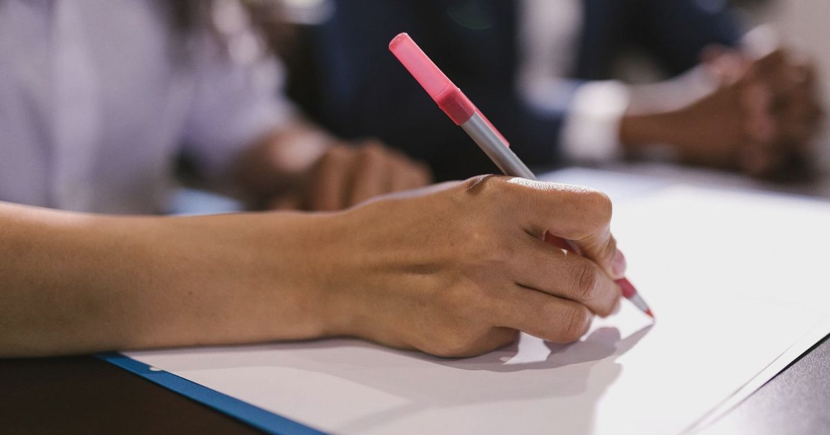Detailed close-up of a person writing on paper with a pen in an office setting.