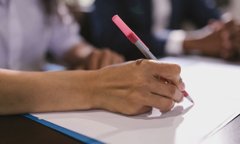 Detailed close-up of a person writing on paper with a pen in an office setting.