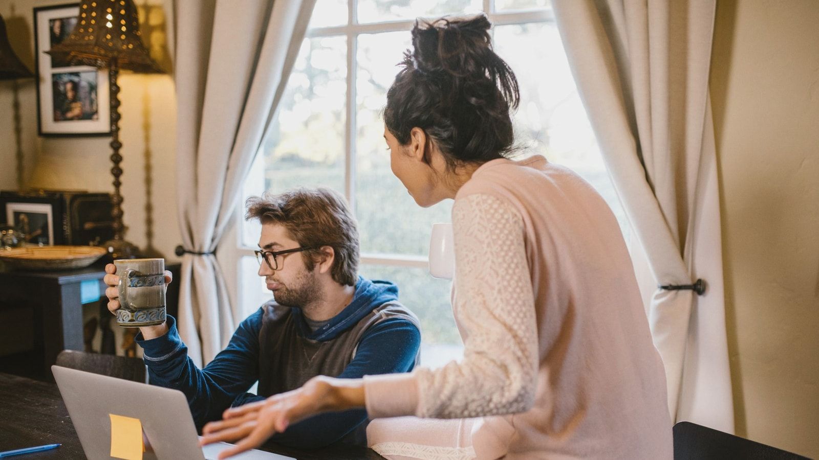 A couple engaged in a heated discussion indoors with a laptop open on the table.