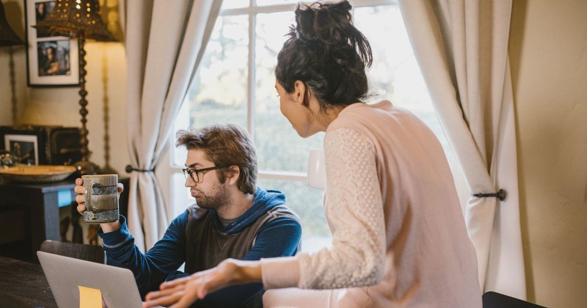 A couple engaged in a heated discussion indoors with a laptop open on the table.