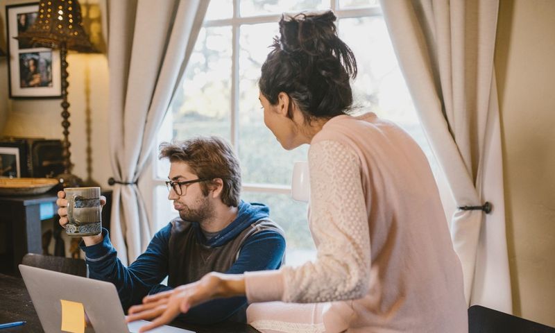 A couple engaged in a heated discussion indoors with a laptop open on the table.