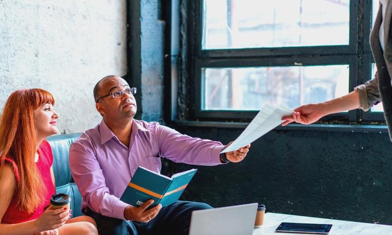 A group of professionals working together in a modern office setting, exchanging documents and ideas.