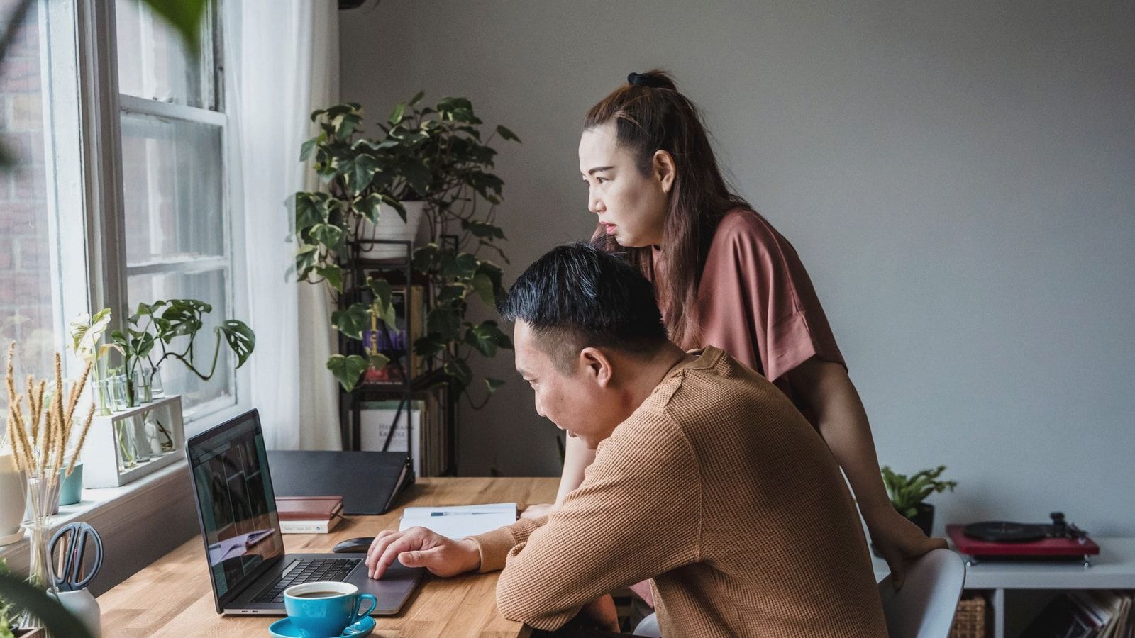 Asian couple working together at a home office, focused on a laptop screen, indoors.