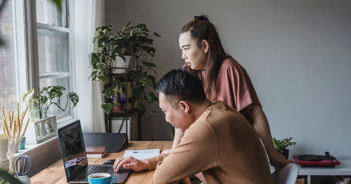 Asian couple working together at a home office, focused on a laptop screen, indoors.