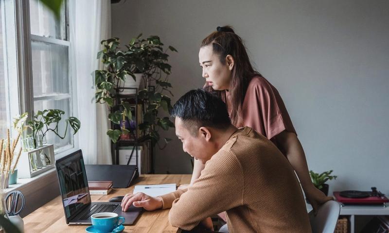 Asian couple working together at a home office, focused on a laptop screen, indoors.