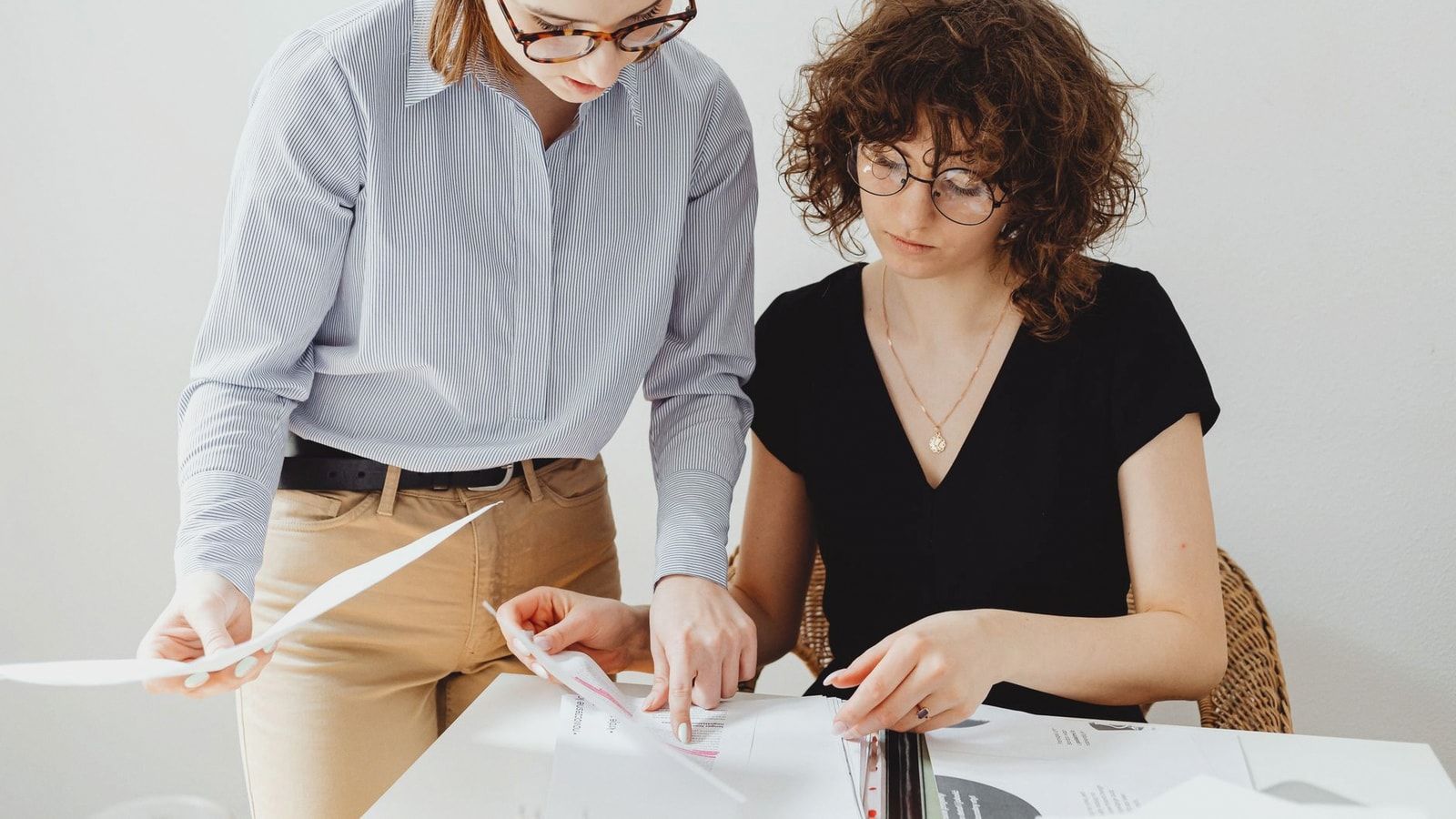 Two businesswomen reviewing documents at a workspace, focusing on collaboration and teamwork.