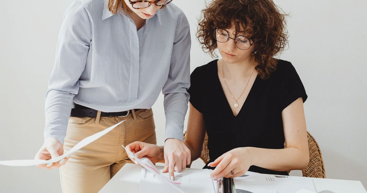 Two businesswomen reviewing documents at a workspace, focusing on collaboration and teamwork.