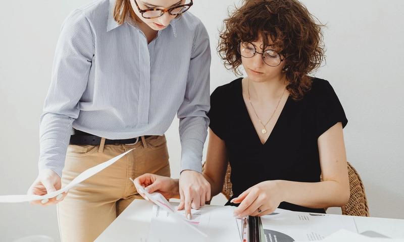 Two businesswomen reviewing documents at a workspace, focusing on collaboration and teamwork.