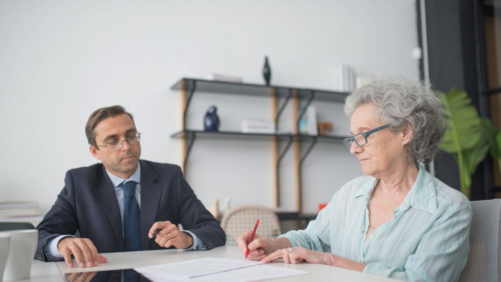 Elderly woman signing paperwork in modern office with consultant.