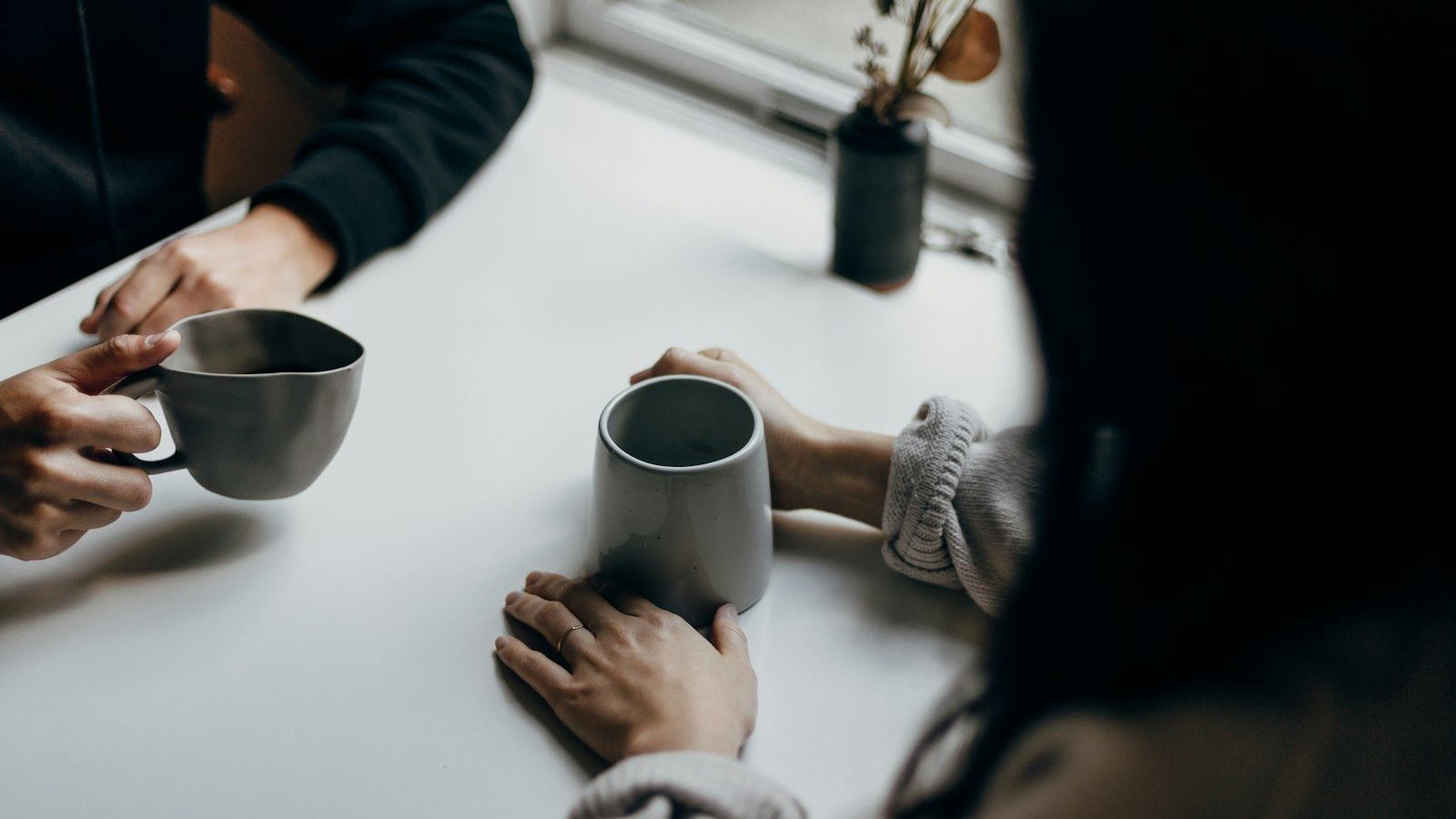 two people holding gray mugs at table
