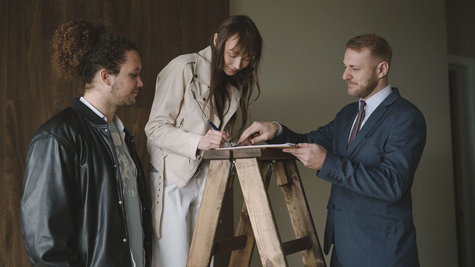 Three individuals signing a contract on a ladder inside a new house, symbolizing a real estate deal.