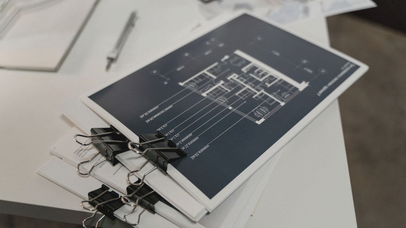 Stack of architectural floor plans bound with clips on a white table, ideal for design projects.