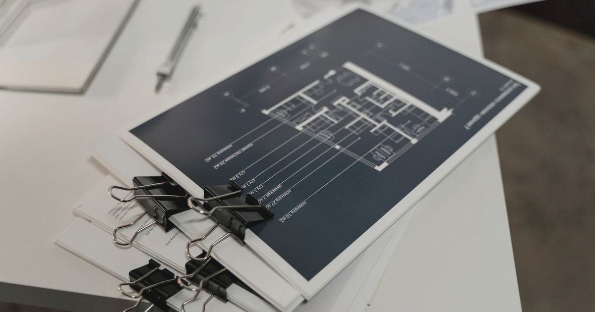 Stack of architectural floor plans bound with clips on a white table, ideal for design projects.