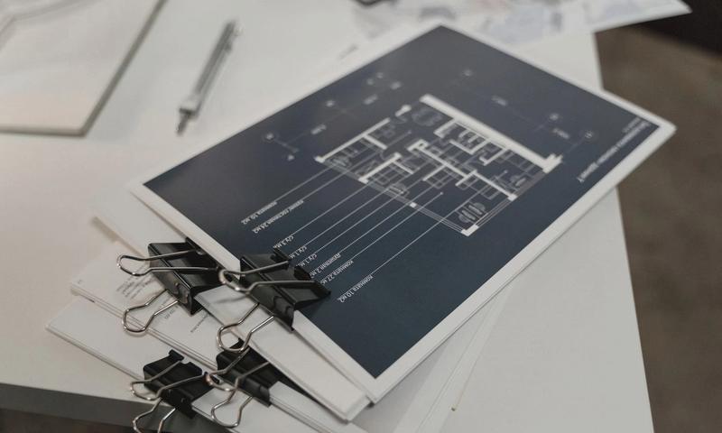 Stack of architectural floor plans bound with clips on a white table, ideal for design projects.