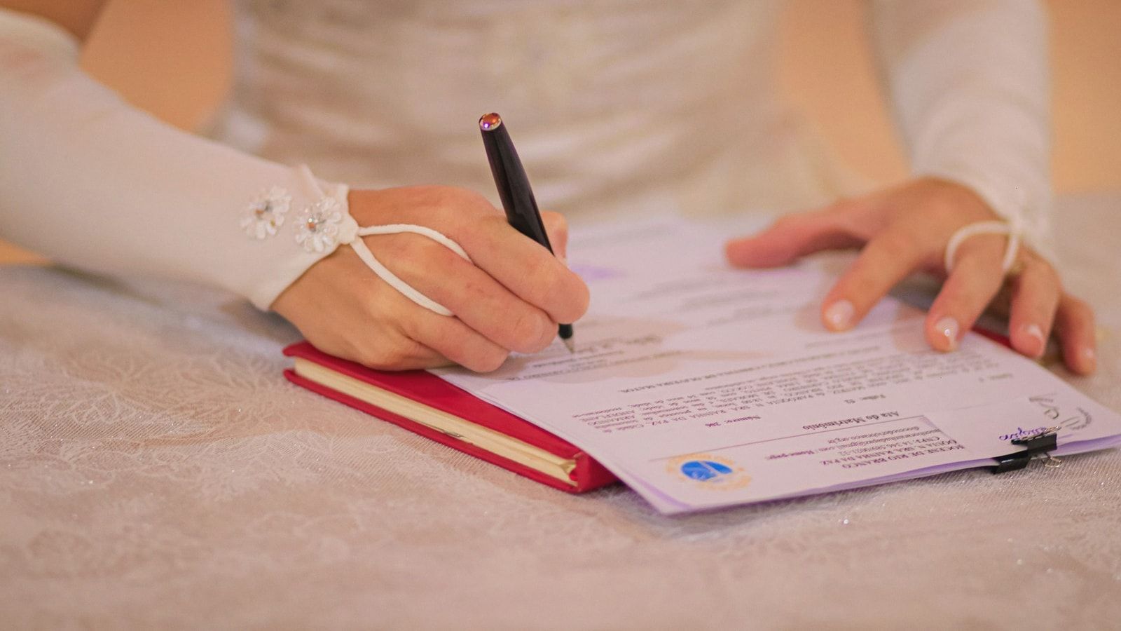 Close-up of a bride signing her wedding certificate at a ceremony.