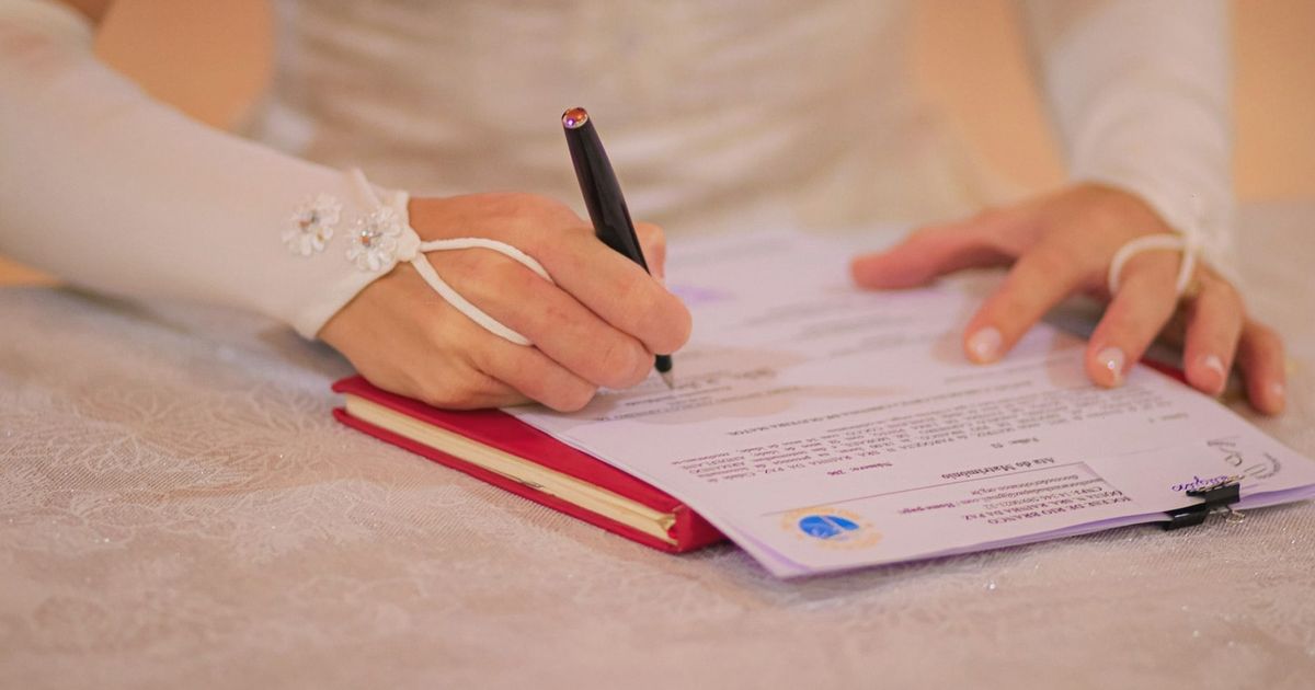 Close-up of a bride signing her wedding certificate at a ceremony.