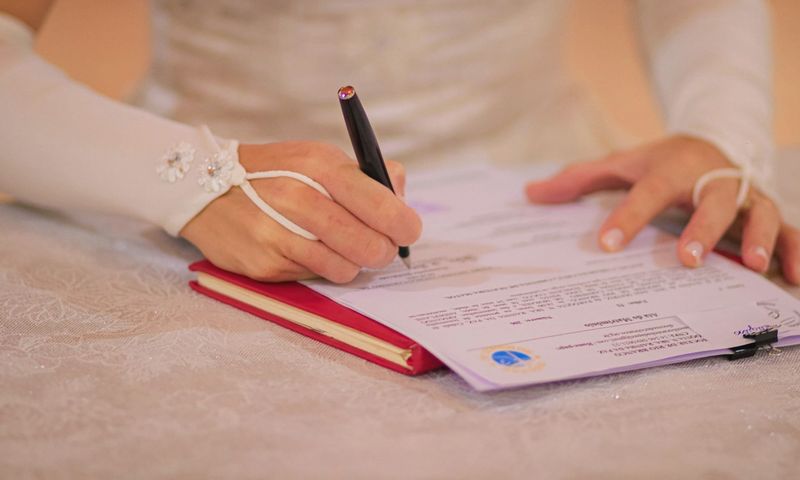 Close-up of a bride signing her wedding certificate at a ceremony.