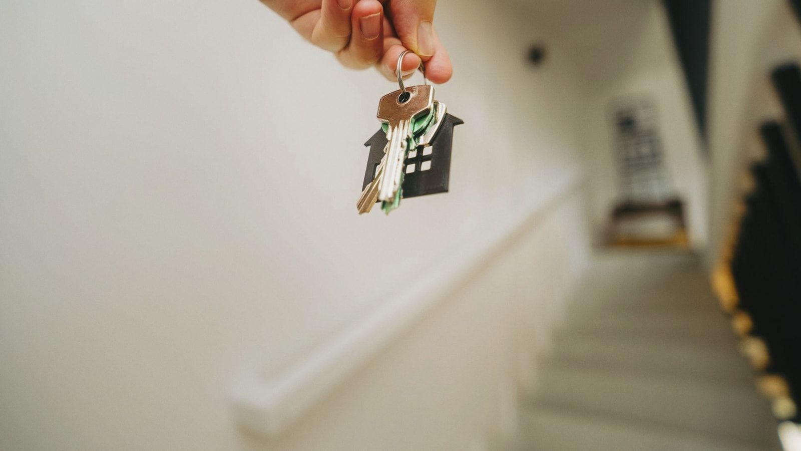 Close-up of a hand holding a keychain in the shape of a house, symbolizing real estate and property ownership.