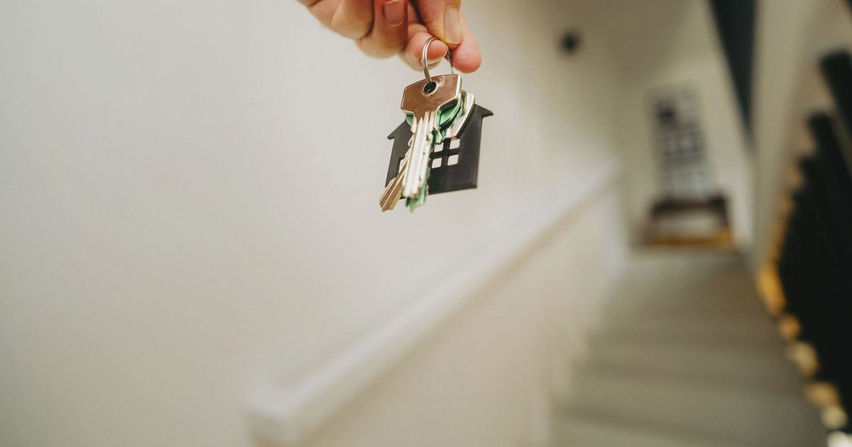 Close-up of a hand holding a keychain in the shape of a house, symbolizing real estate and property ownership.