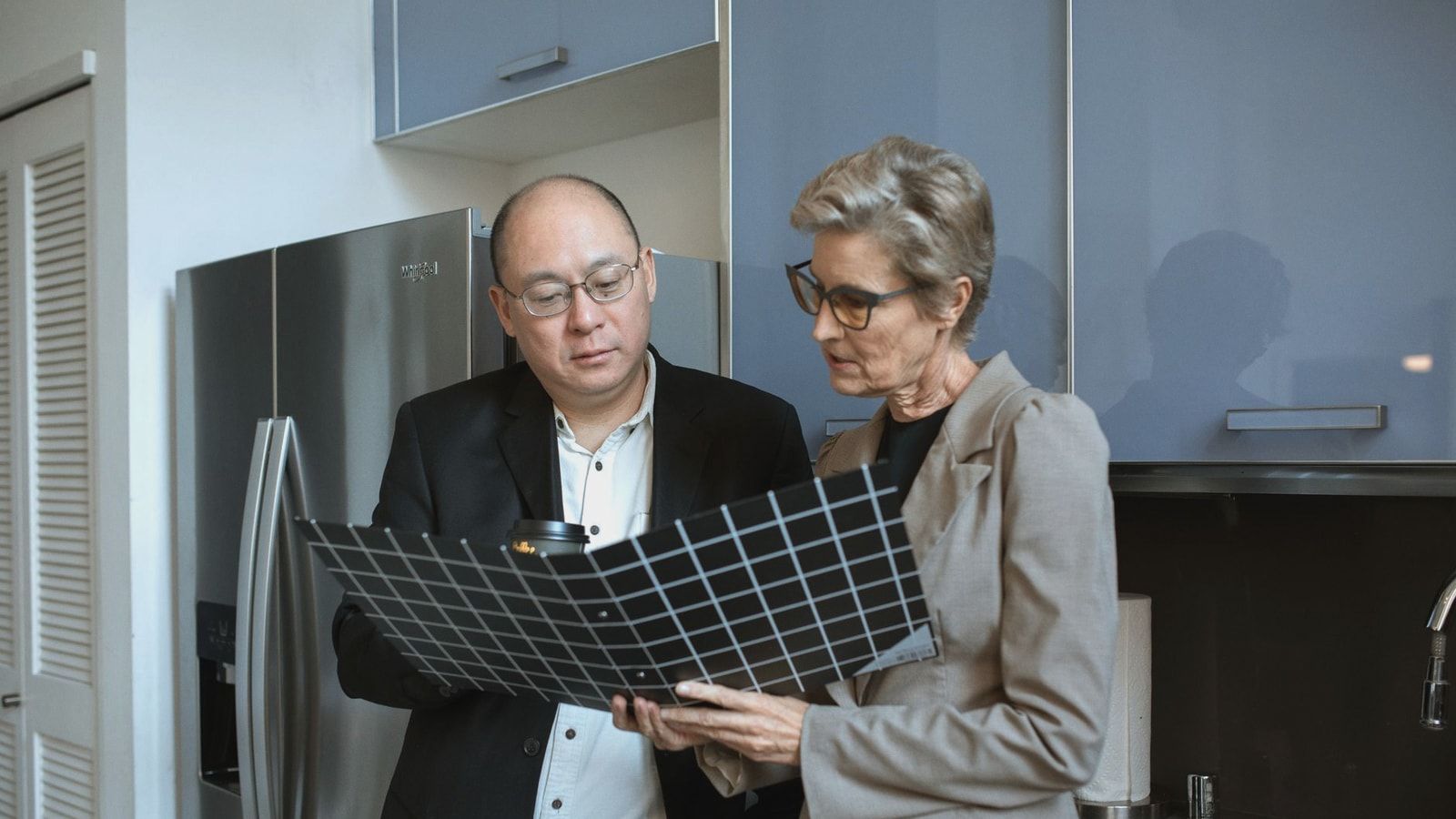 Two business professionals review documents in a modern office kitchen setting.