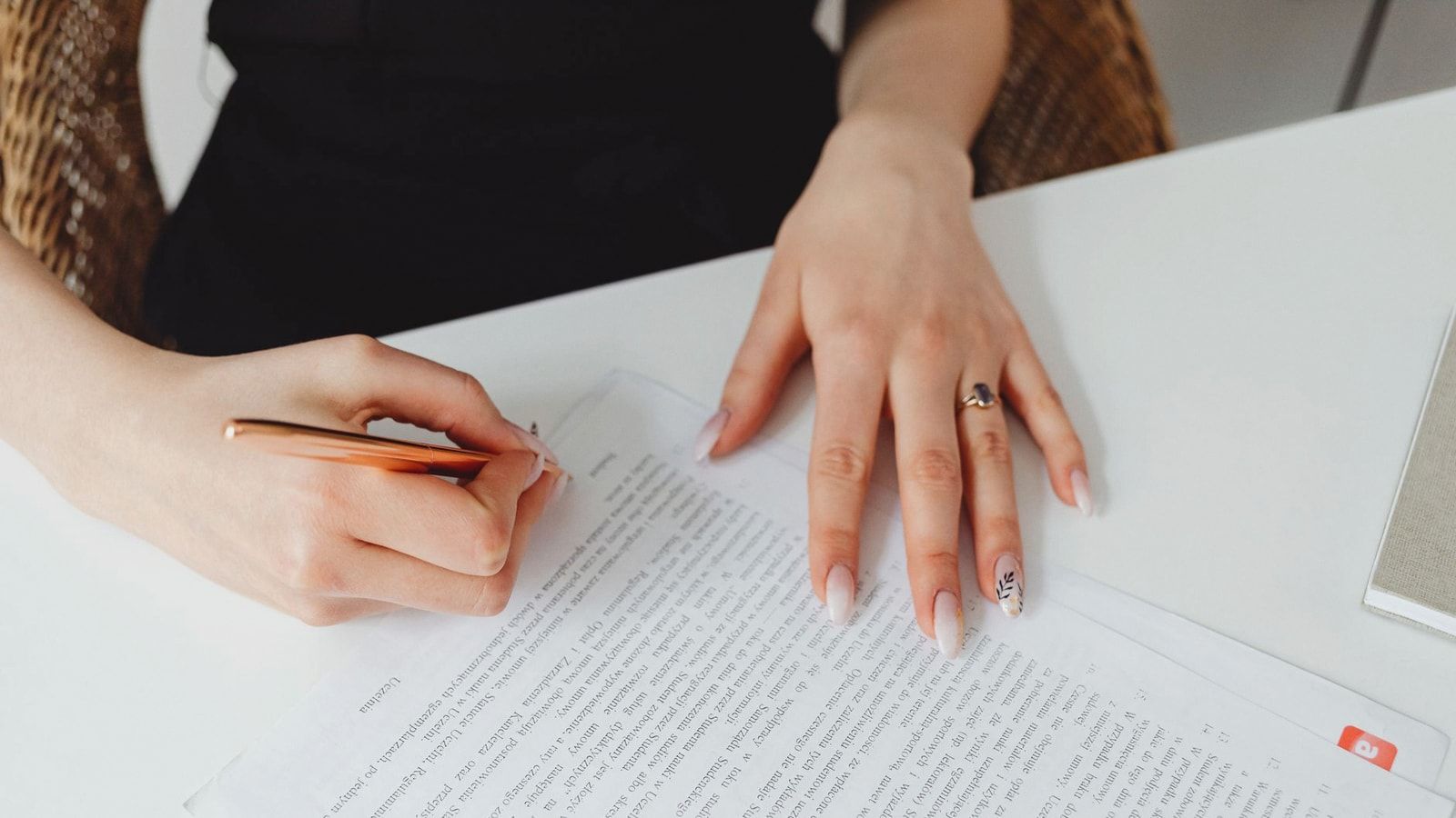 A woman signing a document with a pen on a desk, emphasizing hands and writing.