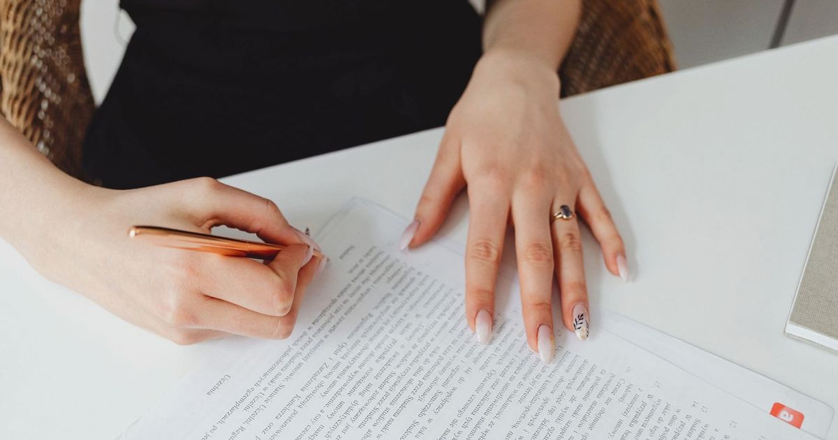 A woman signing a document with a pen on a desk, emphasizing hands and writing.