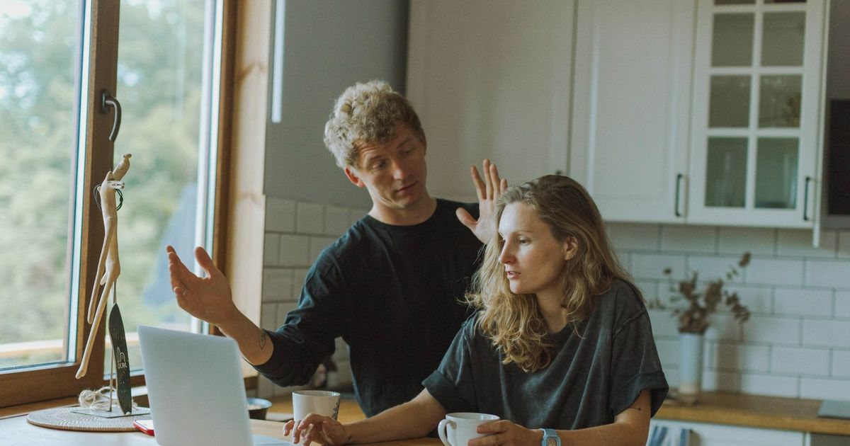 A couple interacting in a bright kitchen using a laptop at a wooden counter.