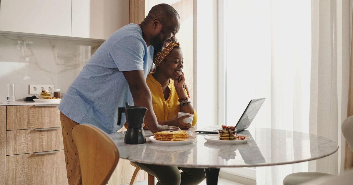 A joyful couple sharing breakfast and working on a laptop in their cozy kitchen.