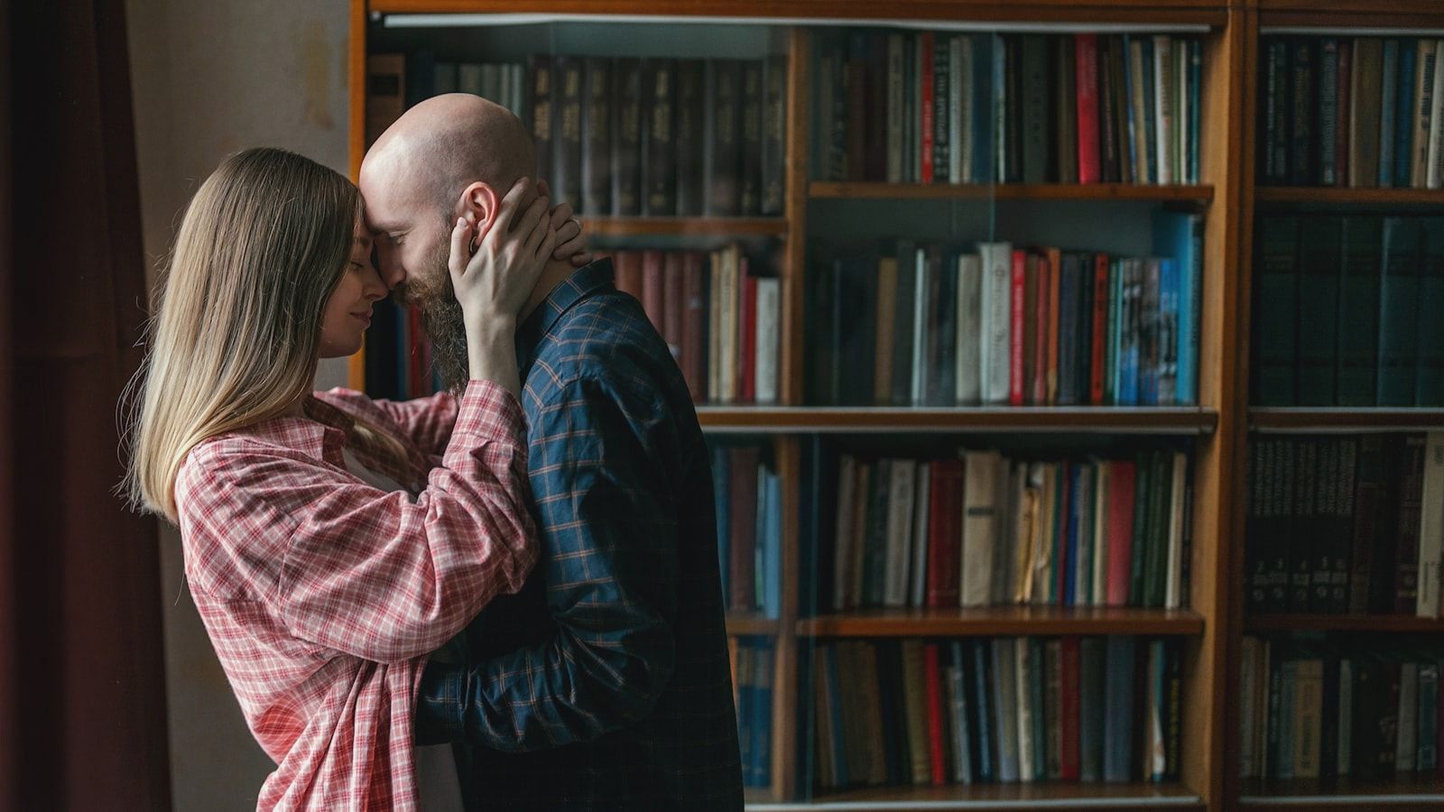 A man and woman kissing in front of a bookcase