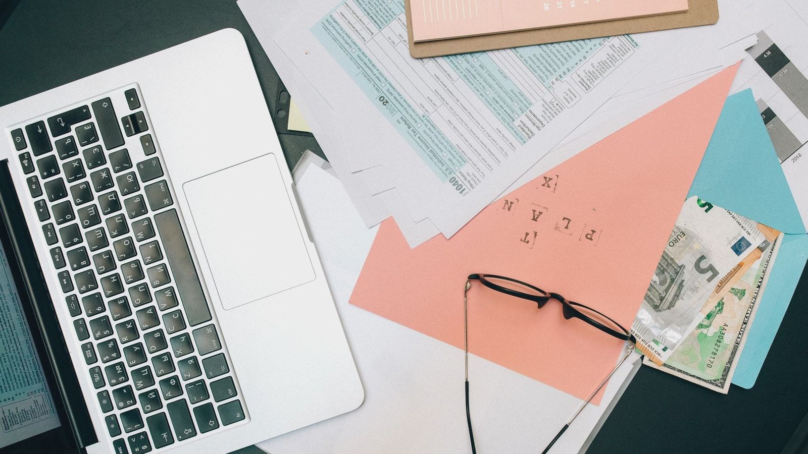 A tidy workspace featuring a laptop, documents, and eyeglasses for productivity.
