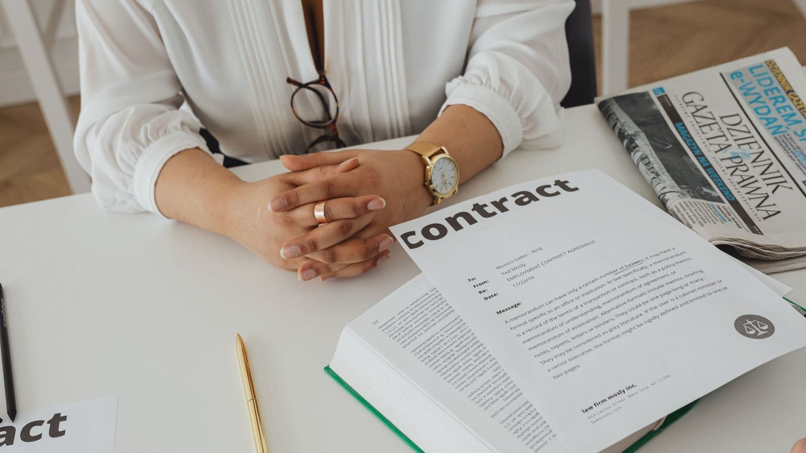 Businesswoman sitting at desk reviewing contract with legal documents and newspaper.