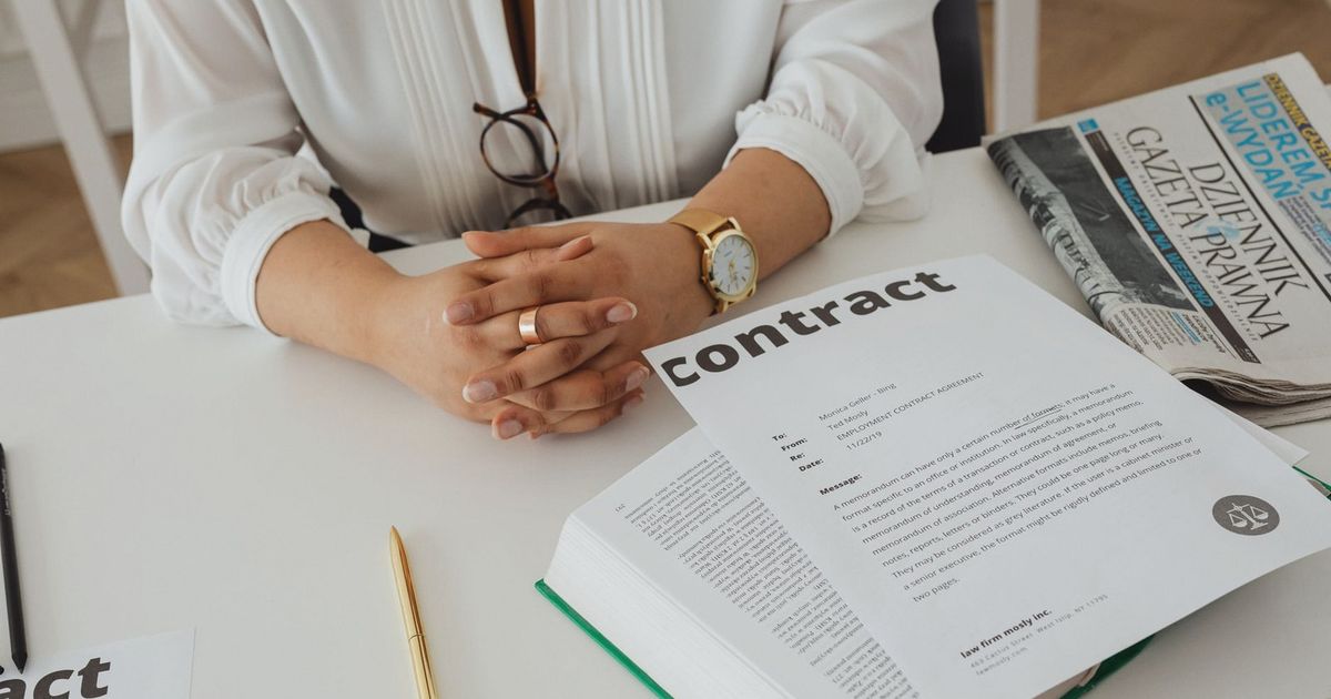 Businesswoman sitting at desk reviewing contract with legal documents and newspaper.