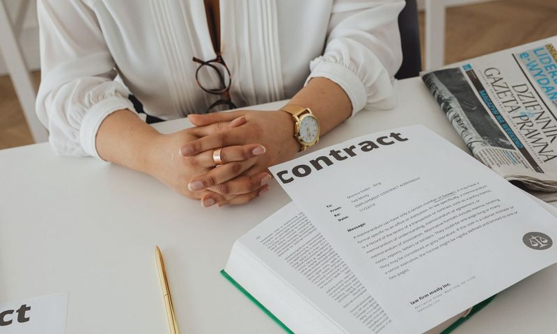 Businesswoman sitting at desk reviewing contract with legal documents and newspaper.