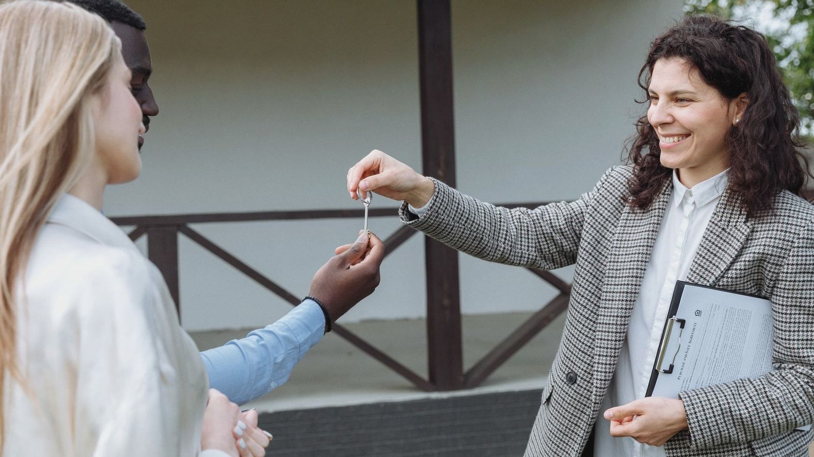 Real estate agent giving house keys to a happy couple outside their new home.