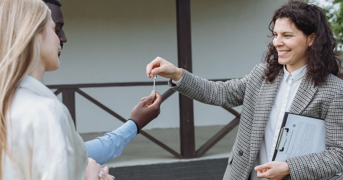 Real estate agent giving house keys to a happy couple outside their new home.