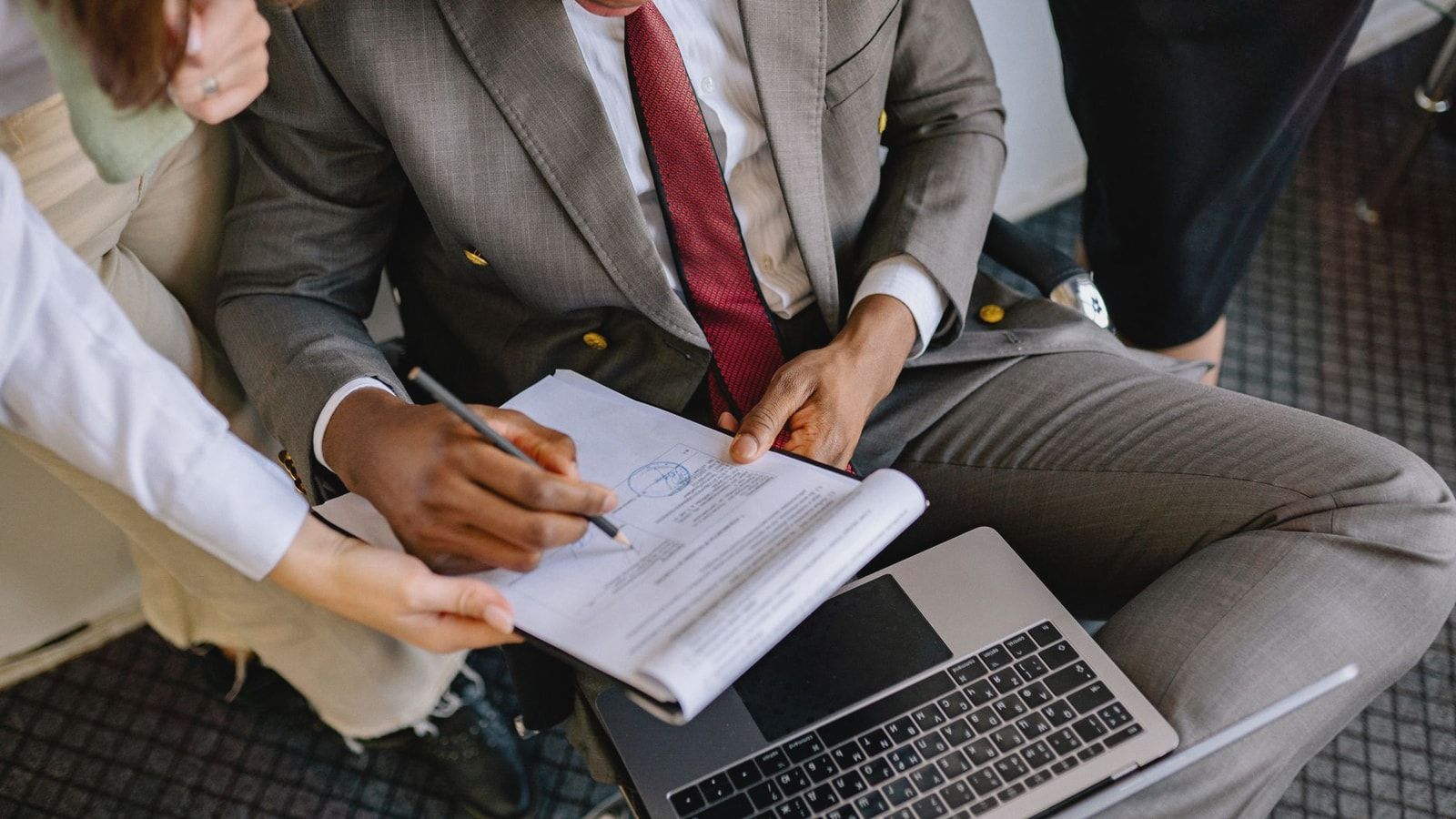A businessman in a suit signing a contract with colleagues' assistance.