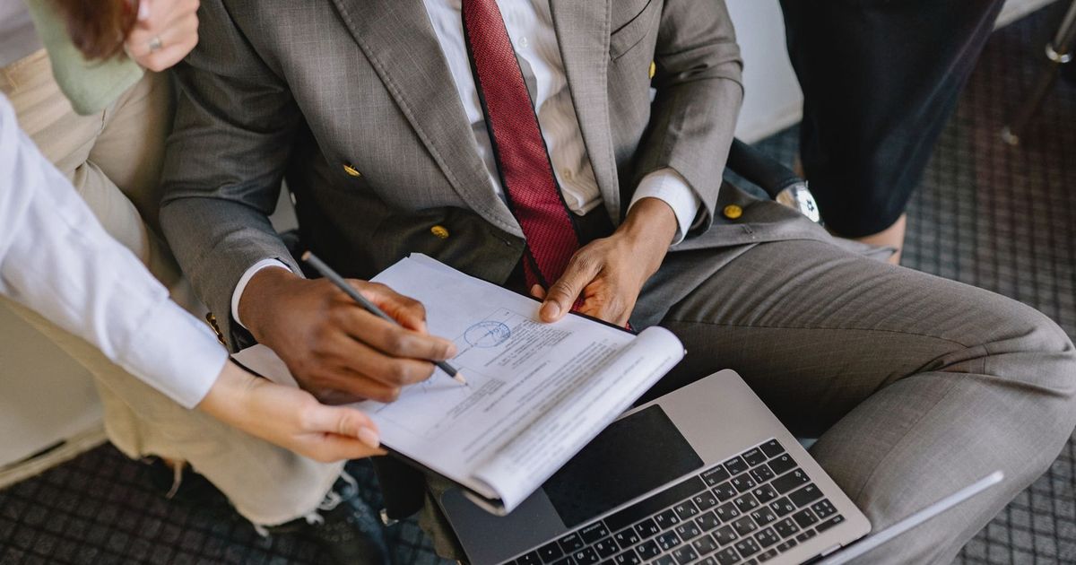 A businessman in a suit signing a contract with colleagues' assistance.
