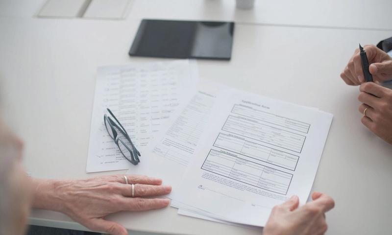 Close-up view of two individuals reviewing documents and forms in an office setting.