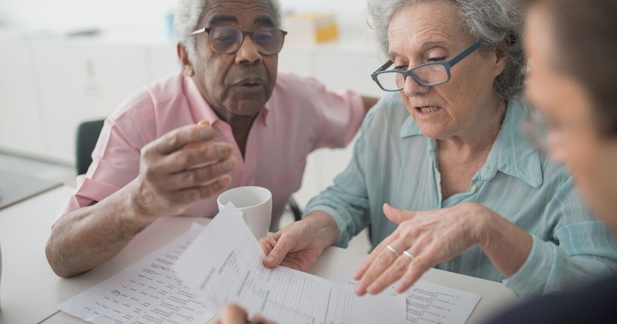 Elderly couple discussing financial documents with a consultant in an office setting.