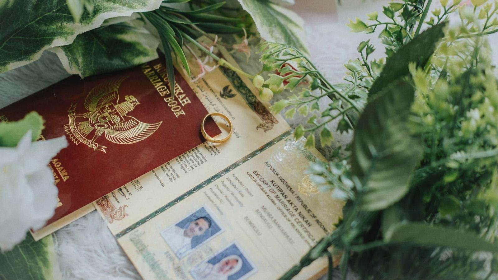 Close-up of marriage book and certificate adorned with greenery and wedding ring.