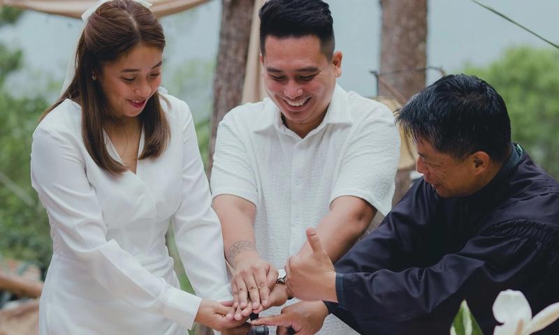 A joyful couple finalizing their wedding with the officiant outdoors.