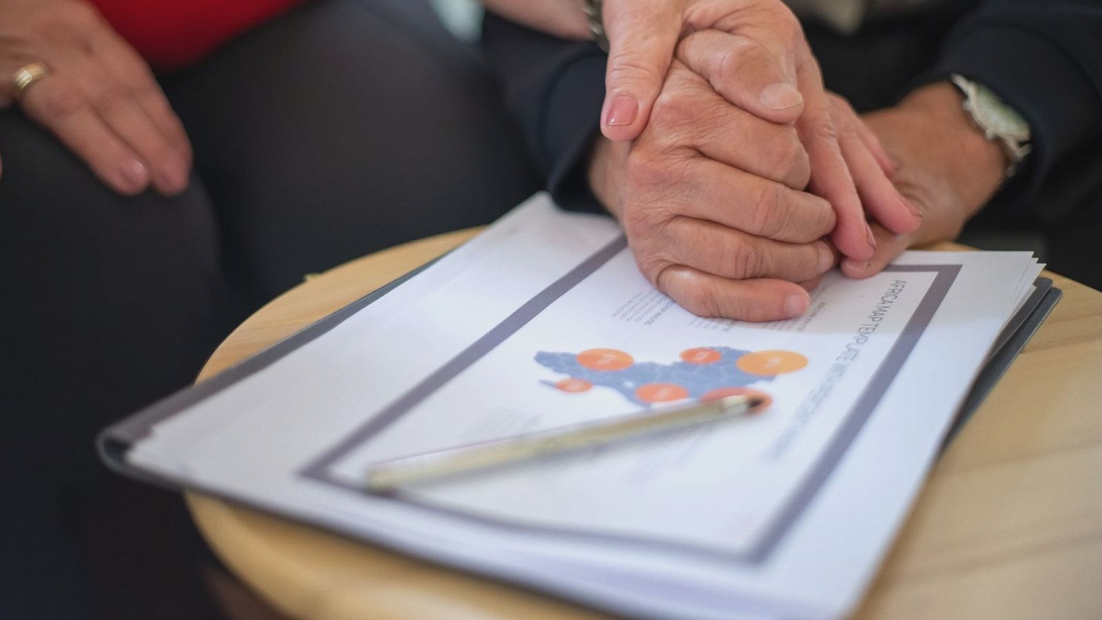 Two adults holding hands over business documents, symbolizing support and partnership.