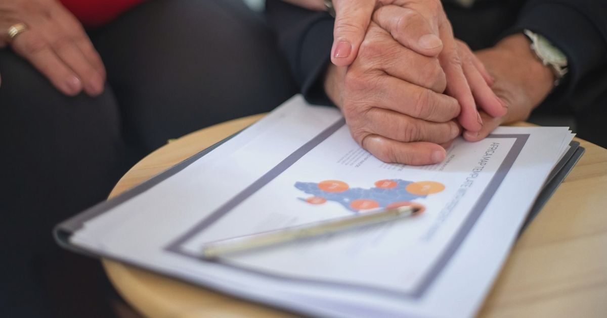 Two adults holding hands over business documents, symbolizing support and partnership.