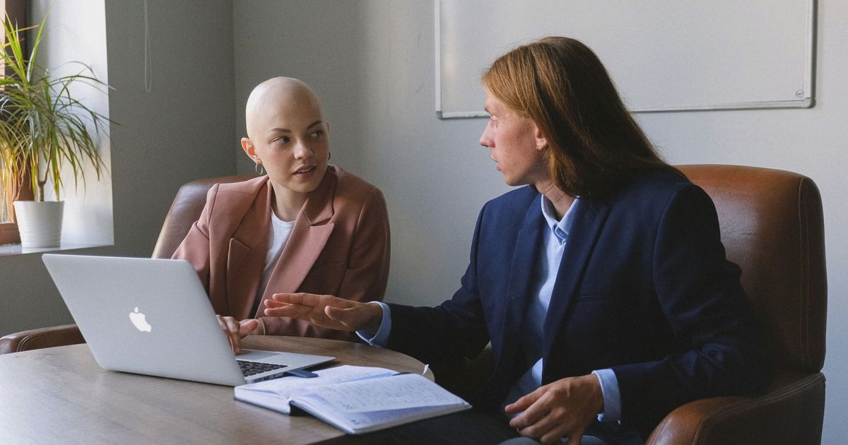 Confident young coworkers wearing formal jackets sitting in leather armchairs near table with netbook and organizer while sharing business ideas